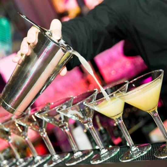 Bartender pouring drinks into a line of cocktail glasses